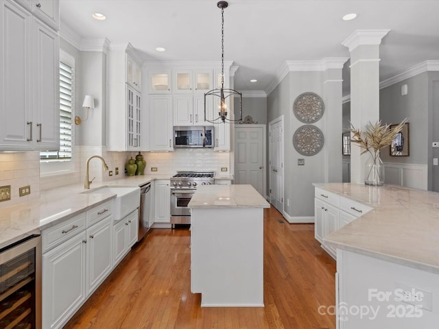 kitchen featuring beverage cooler, a kitchen island, a sink, white cabinetry, and appliances with stainless steel finishes