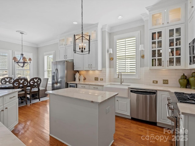 kitchen with white cabinets, appliances with stainless steel finishes, ornamental molding, an inviting chandelier, and a sink