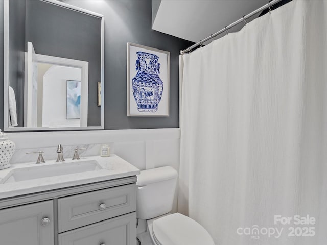 full bathroom featuring wainscoting, vanity, toilet, and a decorative wall