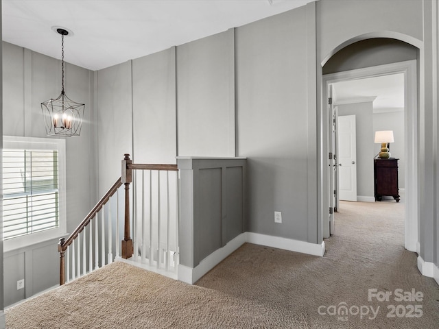 hallway with carpet flooring, a decorative wall, an upstairs landing, and an inviting chandelier