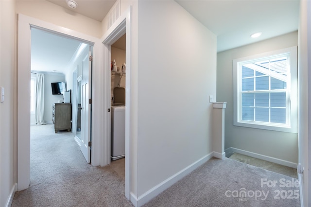 hall with a healthy amount of sunlight, washer / dryer, baseboards, and light colored carpet