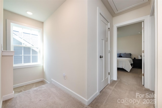 hallway with attic access, baseboards, and light colored carpet