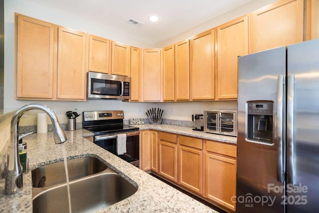 kitchen featuring appliances with stainless steel finishes, light brown cabinets, a sink, and light stone countertops