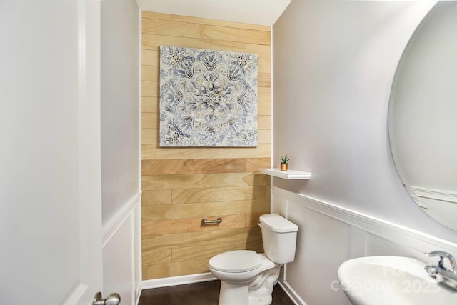 bathroom featuring wainscoting, a sink, toilet, and a decorative wall