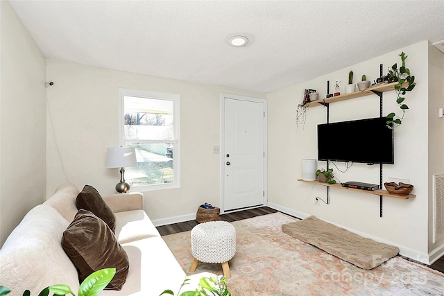 living area with a textured ceiling, wood finished floors, visible vents, and baseboards