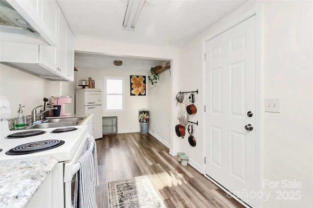 kitchen featuring light wood finished floors, light countertops, white cabinets, a sink, and white appliances