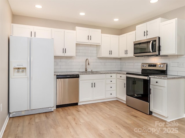 kitchen with stainless steel appliances, light wood finished floors, a sink, and white cabinetry