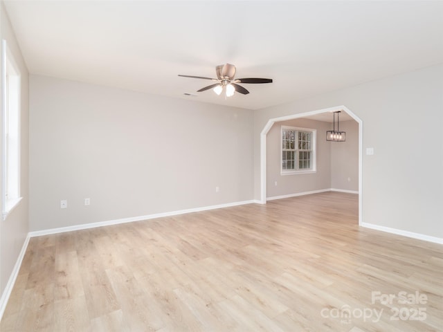 empty room featuring light wood-style floors, baseboards, arched walkways, and ceiling fan with notable chandelier