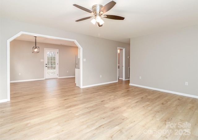 spare room with arched walkways, light wood-type flooring, a ceiling fan, and baseboards