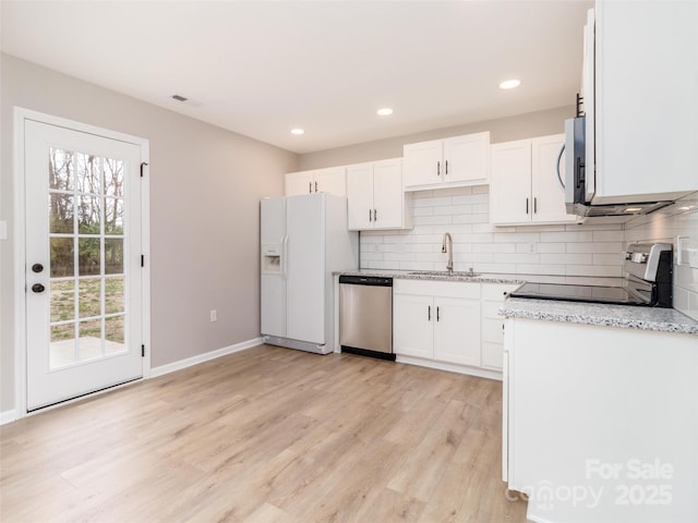 kitchen with tasteful backsplash, appliances with stainless steel finishes, light wood-style floors, white cabinets, and a sink