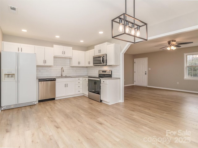 kitchen with a sink, light wood finished floors, stainless steel appliances, and backsplash