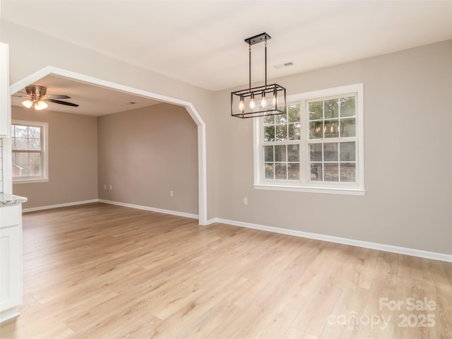 empty room featuring light wood finished floors, visible vents, arched walkways, baseboards, and ceiling fan with notable chandelier