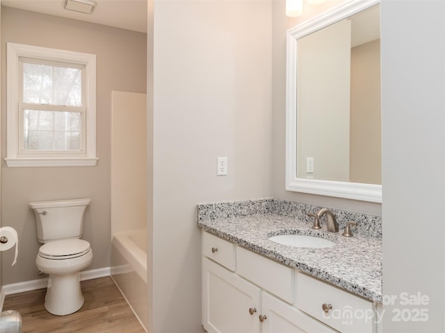 bathroom with toilet, vanity, wood finished floors, baseboards, and a bath