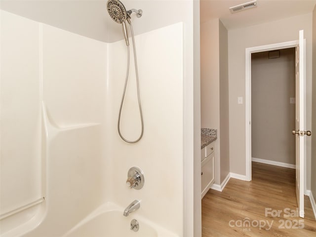 full bath featuring visible vents, shower / bathing tub combination, vanity, wood finished floors, and baseboards