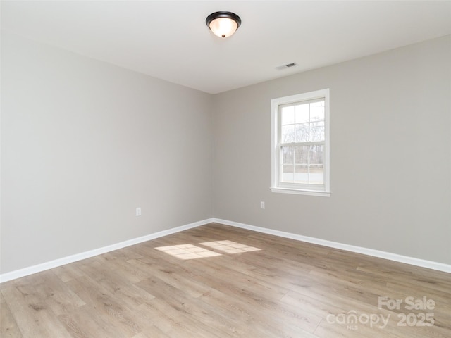 empty room featuring light wood-type flooring, visible vents, and baseboards