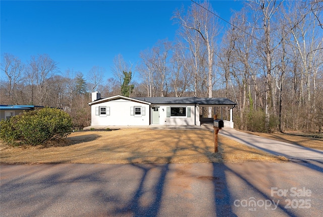 view of front facade with driveway, a chimney, a carport, and stucco siding