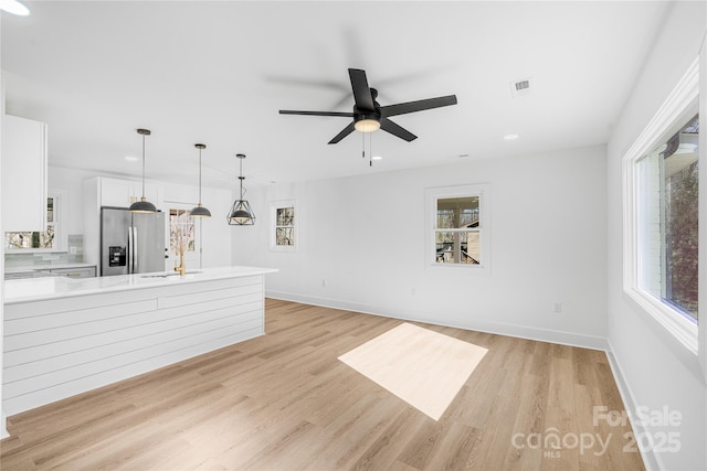 unfurnished living room with plenty of natural light, a sink, light wood-style flooring, and baseboards