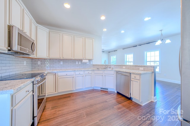 kitchen featuring a peninsula, a sink, appliances with stainless steel finishes, light wood-type flooring, and tasteful backsplash