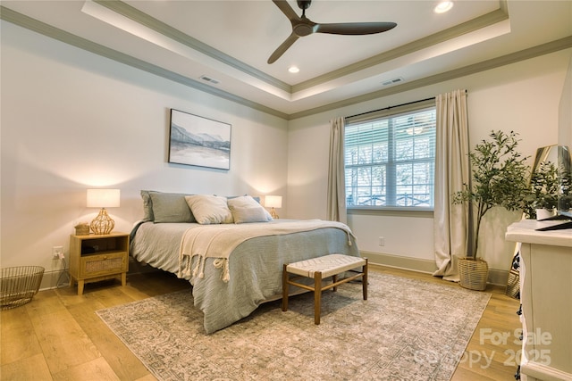 bedroom with baseboards, light wood-style floors, a tray ceiling, and ornamental molding