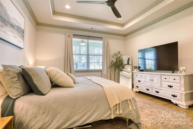 bedroom featuring a ceiling fan, visible vents, a tray ceiling, light wood-style flooring, and crown molding