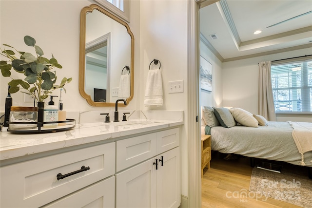 bathroom with vanity, wood finished floors, visible vents, a tray ceiling, and ornamental molding