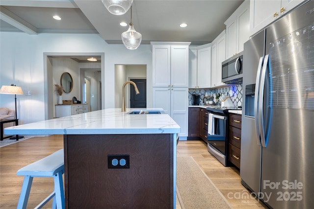 kitchen featuring light wood finished floors, a sink, stainless steel appliances, a kitchen breakfast bar, and backsplash