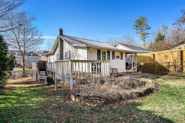 rear view of property featuring fence, a wooden deck, a chimney, central air condition unit, and metal roof