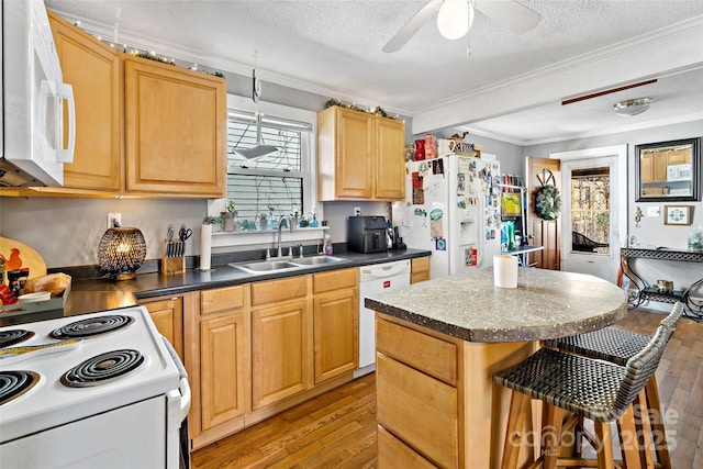 kitchen featuring dark countertops, a breakfast bar area, ornamental molding, white appliances, and a sink