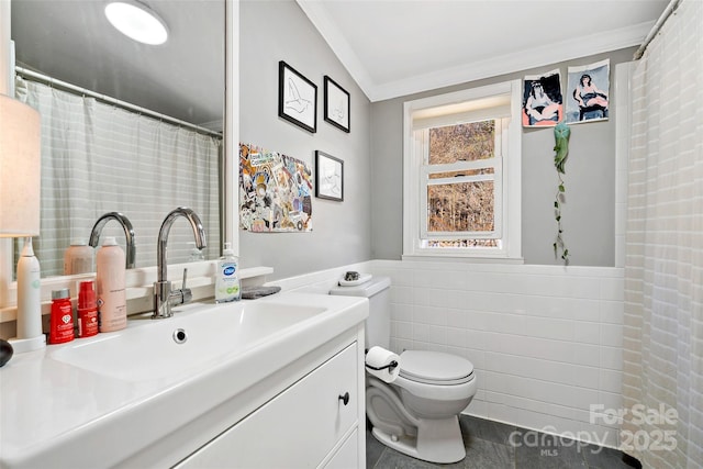 bathroom featuring vanity, ornamental molding, wainscoting, tile walls, and toilet