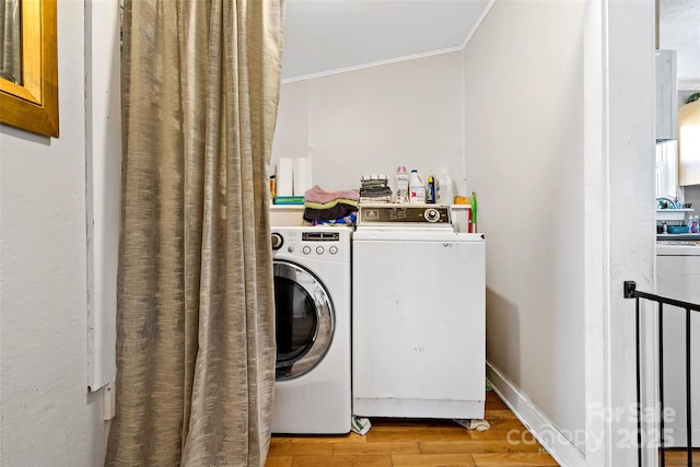 clothes washing area with light wood-type flooring, baseboards, washing machine and dryer, and ornamental molding