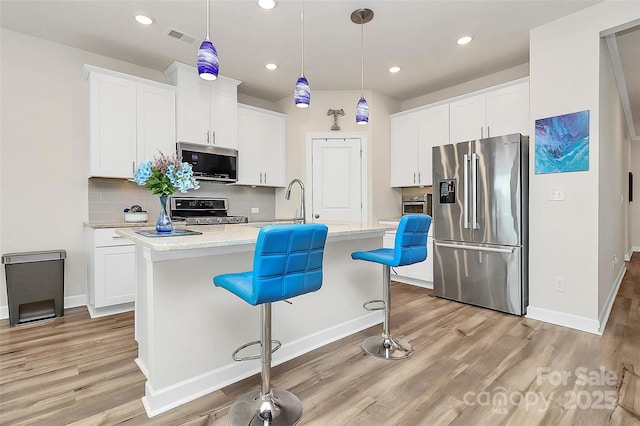 kitchen with stainless steel appliances, visible vents, a center island with sink, and light wood-style flooring