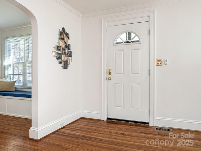 foyer featuring baseboards, arched walkways, crown molding, and wood finished floors