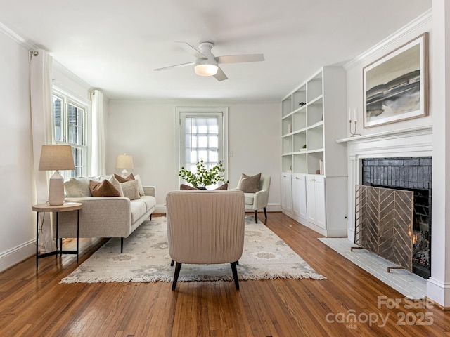 living room with ceiling fan, a fireplace with flush hearth, baseboards, ornamental molding, and hardwood / wood-style floors