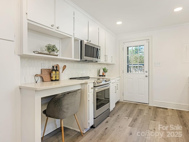 kitchen featuring light wood-style flooring, stainless steel appliances, white cabinetry, ornamental molding, and tasteful backsplash