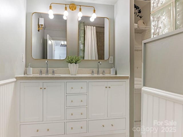 bathroom with double vanity, a spacious closet, wainscoting, and a sink