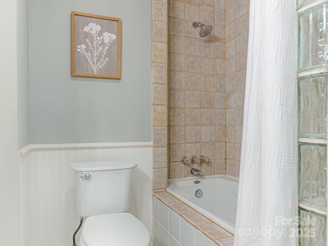 bathroom featuring tiled shower / bath combo, toilet, and wainscoting