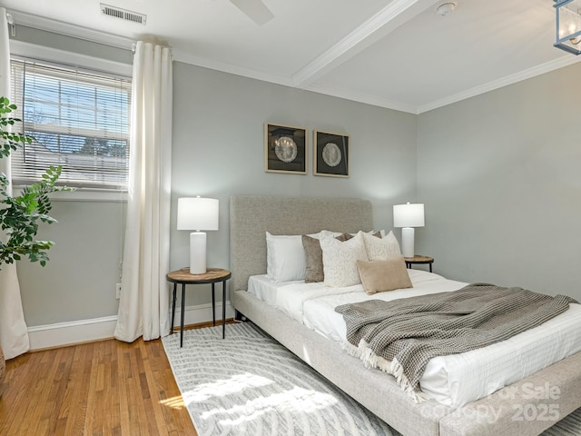 bedroom with baseboards, visible vents, wood finished floors, and ornamental molding