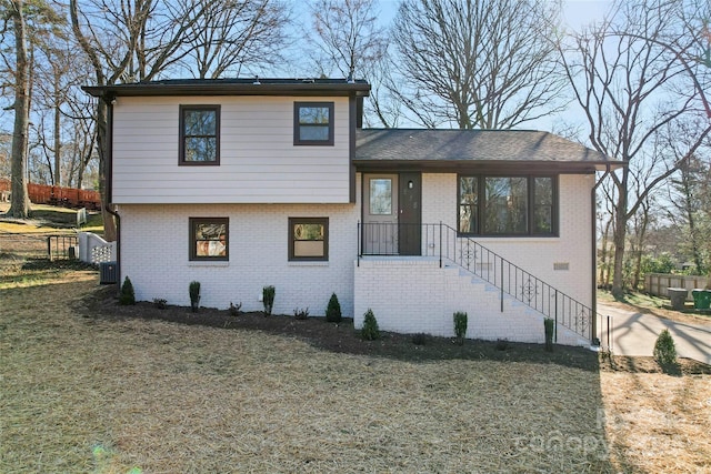 tri-level home featuring cooling unit, brick siding, and fence