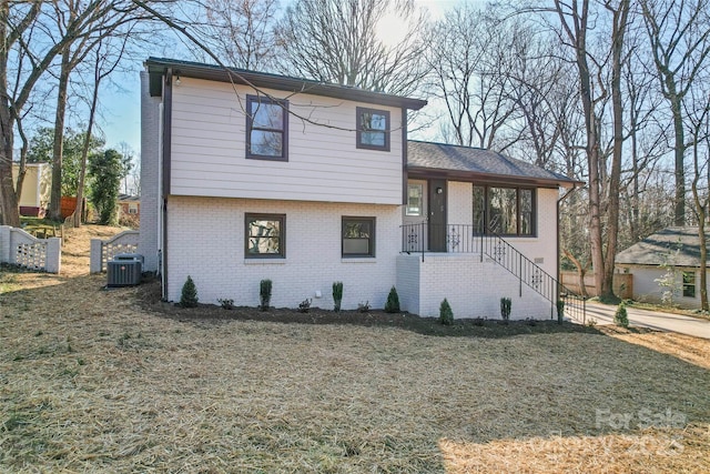 tri-level home with cooling unit, brick siding, and a front yard