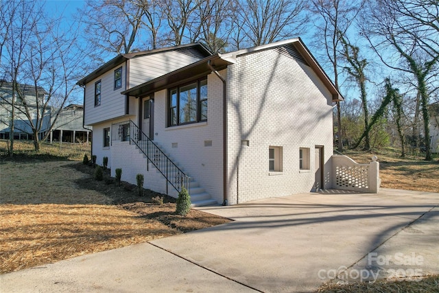 view of front of home featuring stairs, concrete driveway, and brick siding