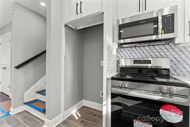 kitchen with stainless steel appliances, tasteful backsplash, wood tiled floor, white cabinetry, and baseboards