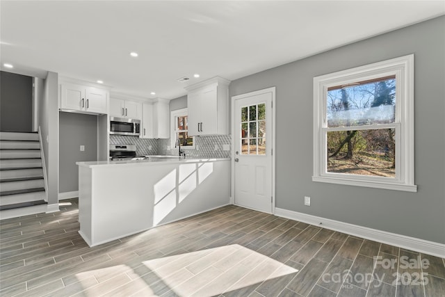 kitchen with stainless steel appliances, tasteful backsplash, wood tiled floor, white cabinetry, and a peninsula