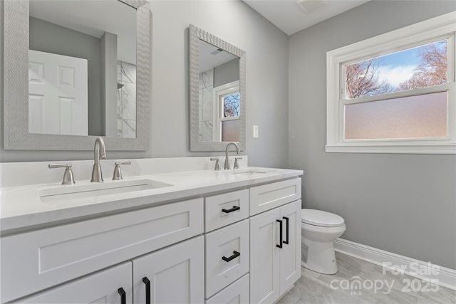 bathroom with toilet, a wealth of natural light, double vanity, and a sink