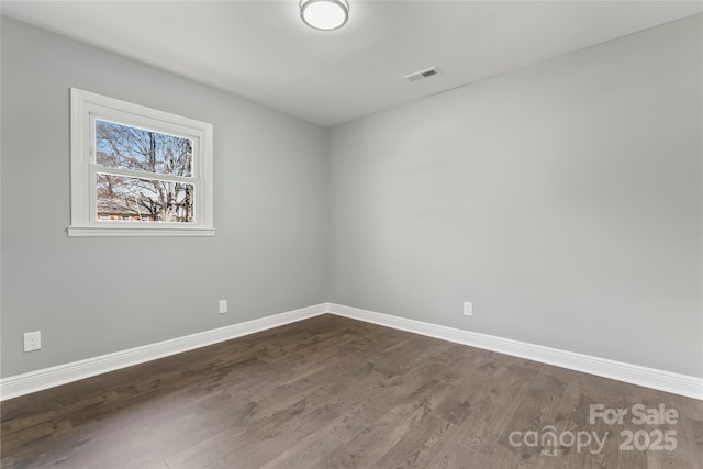 unfurnished room with dark wood-style floors, visible vents, and baseboards