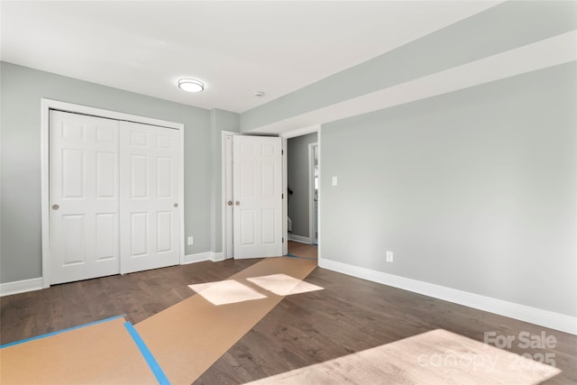 unfurnished bedroom with a closet, wood finished floors, and baseboards