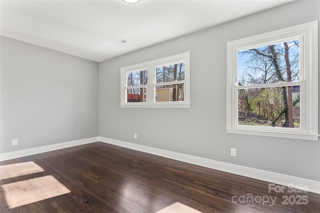 spare room with dark wood finished floors, visible vents, and baseboards