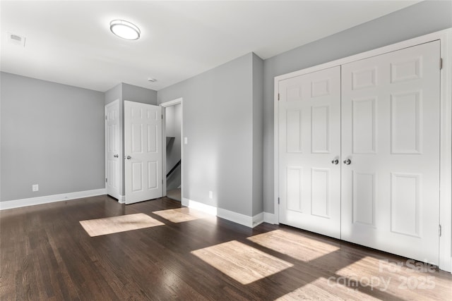 unfurnished bedroom featuring dark wood-type flooring, a closet, visible vents, and baseboards