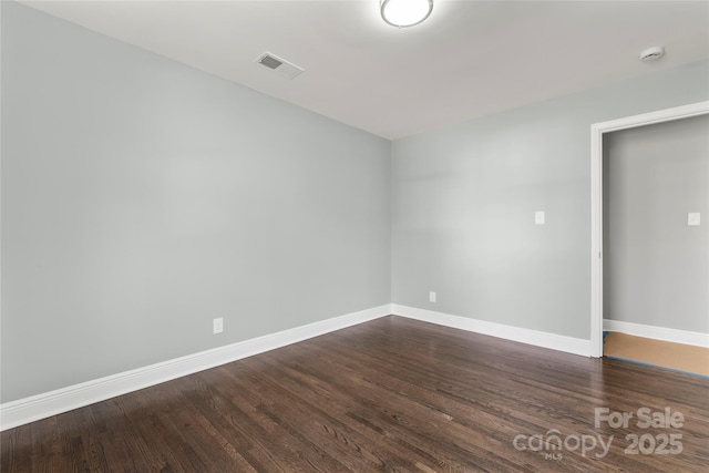 empty room with dark wood-style floors, visible vents, and baseboards