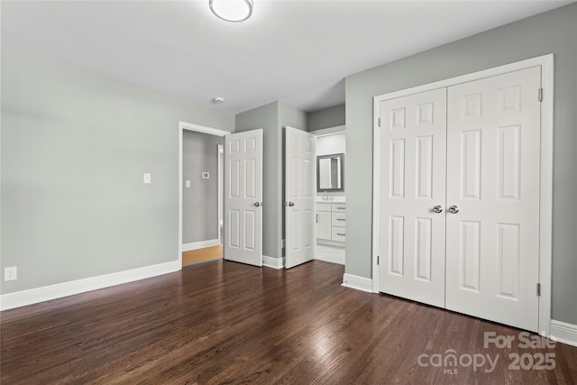 unfurnished bedroom featuring a closet, ensuite bathroom, baseboards, and wood finished floors