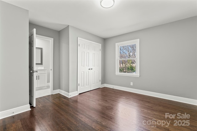 unfurnished bedroom with a closet, baseboards, and dark wood-style flooring